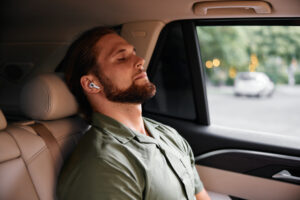 Man relaxing in a car, wearing wireless earbuds, eyes closed, peaceful expression, soft interior lighting